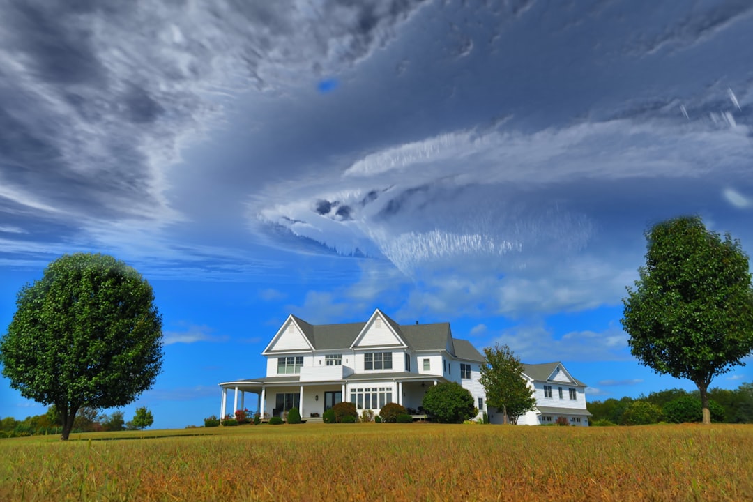 Photo by JOSHUA COLEMAN white and gray house between two green tall trees under gray clouds forming swirl during daytime